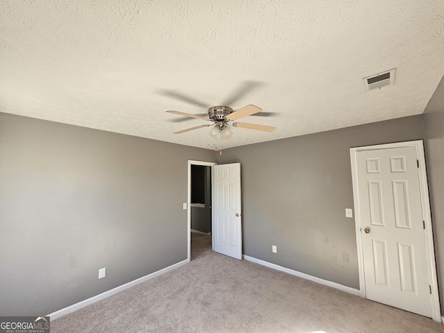 unfurnished bedroom featuring ceiling fan, light carpet, and a textured ceiling