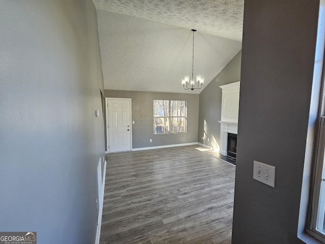 unfurnished living room with lofted ceiling, a chandelier, hardwood / wood-style floors, and a textured ceiling