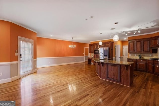 kitchen featuring a breakfast bar area, a center island with sink, ornamental molding, pendant lighting, and hardwood / wood-style floors