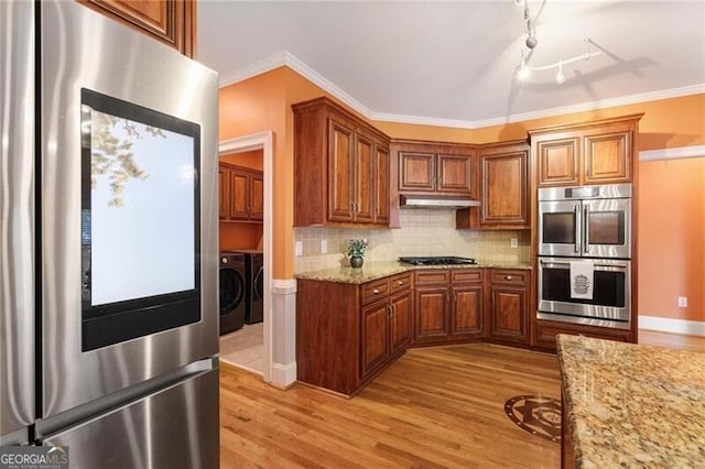 kitchen featuring appliances with stainless steel finishes, backsplash, crown molding, light stone countertops, and washer and clothes dryer