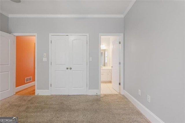 unfurnished bedroom with ornamental molding, light colored carpet, ensuite bathroom, and a closet