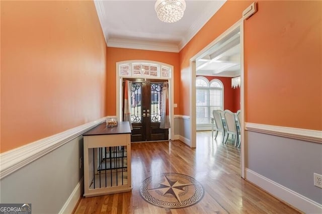 foyer entrance with ornamental molding, hardwood / wood-style floors, a chandelier, and french doors