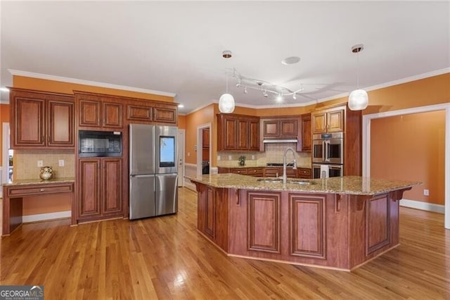 kitchen with sink, a kitchen island with sink, stainless steel appliances, light stone countertops, and decorative light fixtures