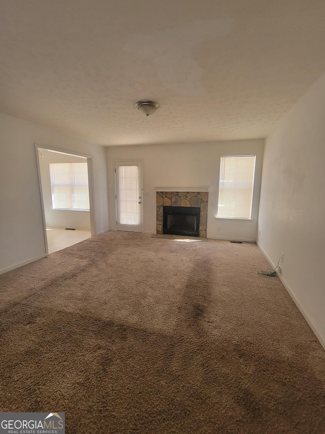 unfurnished living room with a stone fireplace and light colored carpet