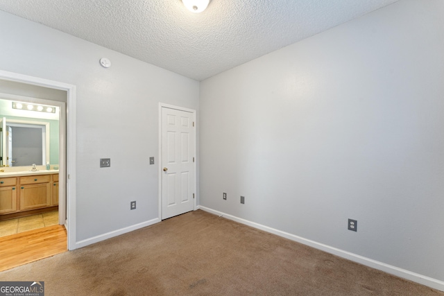 unfurnished bedroom featuring sink, light colored carpet, and a textured ceiling