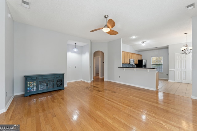 unfurnished living room with ceiling fan with notable chandelier, a textured ceiling, and light wood-type flooring