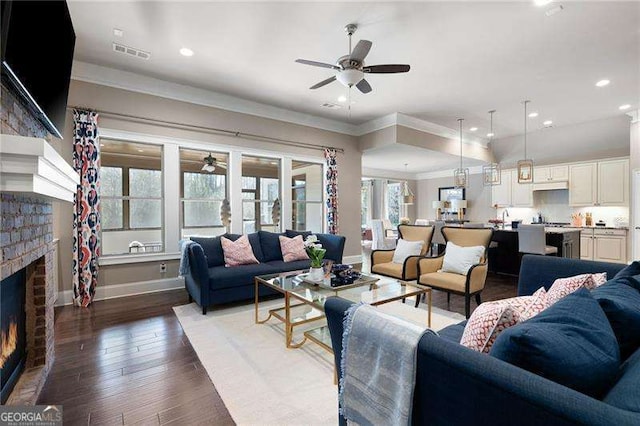 living room featuring ceiling fan, ornamental molding, dark hardwood / wood-style floors, and a fireplace