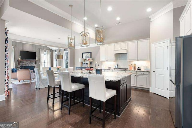 kitchen with dark wood-type flooring, decorative light fixtures, a center island with sink, light stone countertops, and white cabinets