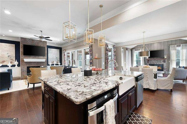 kitchen with sink, hanging light fixtures, stainless steel appliances, a fireplace, and a center island with sink