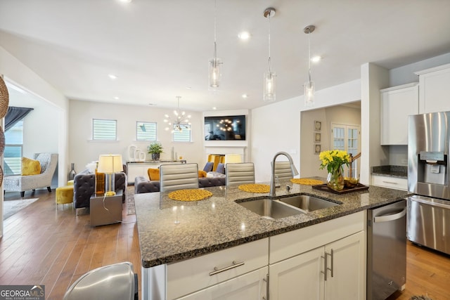 kitchen with appliances with stainless steel finishes, decorative light fixtures, an island with sink, sink, and dark stone countertops