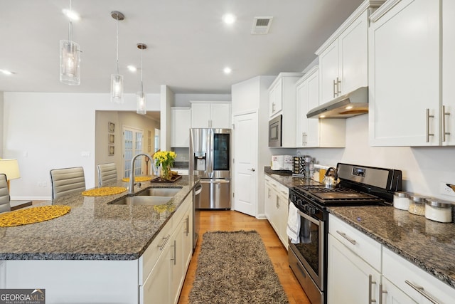 kitchen with pendant lighting, appliances with stainless steel finishes, sink, and an island with sink