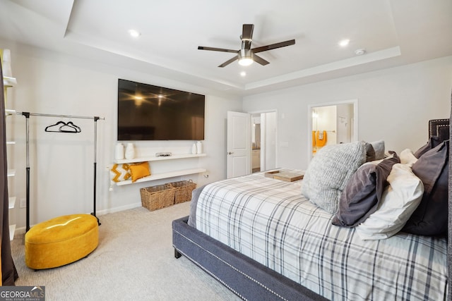 carpeted bedroom with ensuite bathroom, ceiling fan, and a tray ceiling