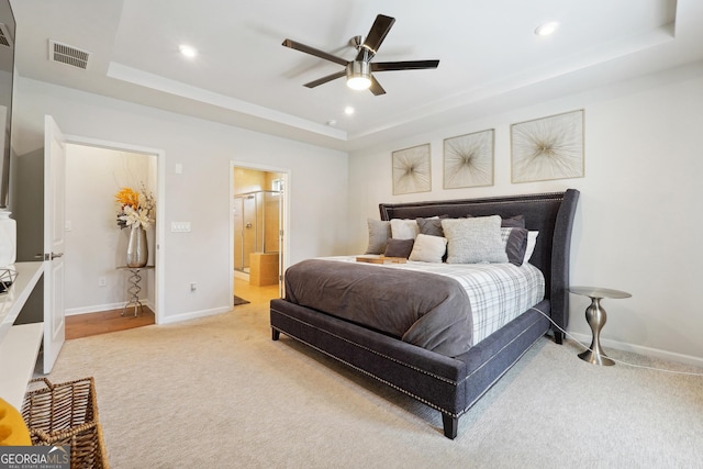 bedroom with light carpet, a raised ceiling, ceiling fan, and ensuite bathroom