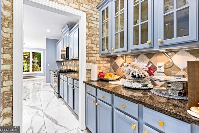 kitchen featuring blue cabinets, stainless steel appliances, dark stone counters, brick wall, and backsplash