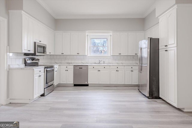 kitchen featuring white cabinetry, tasteful backsplash, ornamental molding, appliances with stainless steel finishes, and light hardwood / wood-style floors