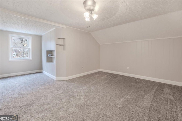 bonus room featuring lofted ceiling, built in features, ceiling fan, carpet flooring, and a textured ceiling