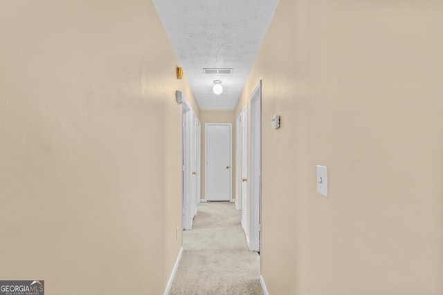 hallway featuring light colored carpet and a textured ceiling