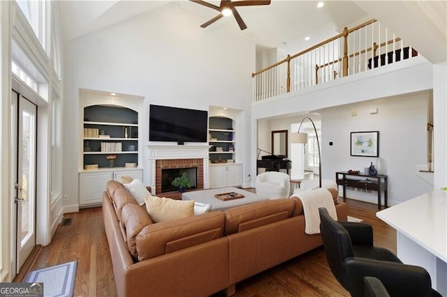 living room featuring wood-type flooring, a fireplace, built in features, and a wealth of natural light