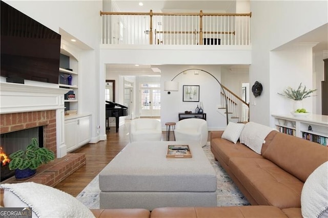 living room with a brick fireplace, a towering ceiling, built in features, and light hardwood / wood-style flooring