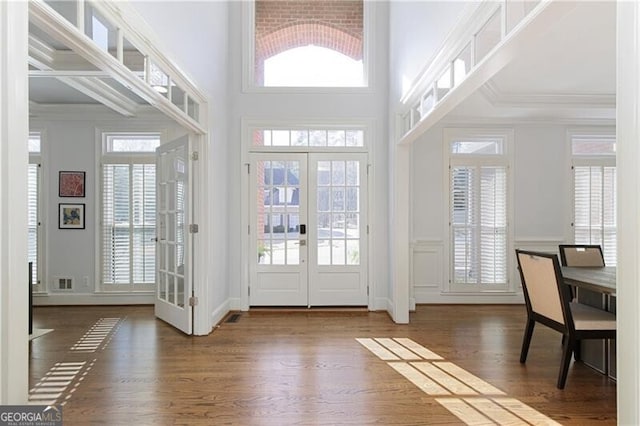 entryway with a towering ceiling, ornamental molding, dark wood-type flooring, and french doors