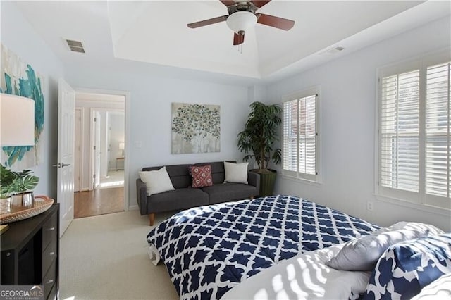 carpeted bedroom with a raised ceiling and ceiling fan