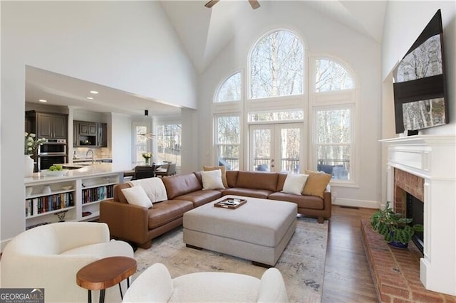 living room featuring high vaulted ceiling, a fireplace, sink, ceiling fan, and light hardwood / wood-style flooring