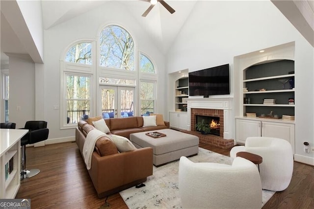 living room with built in features, high vaulted ceiling, dark hardwood / wood-style flooring, a brick fireplace, and french doors