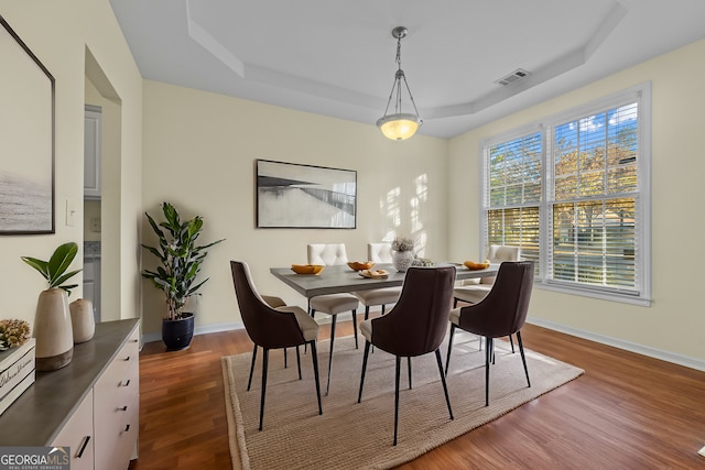 dining room with baseboards, visible vents, a raised ceiling, and wood finished floors