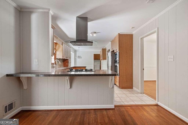 kitchen featuring stainless steel gas stovetop, island exhaust hood, a kitchen bar, and kitchen peninsula