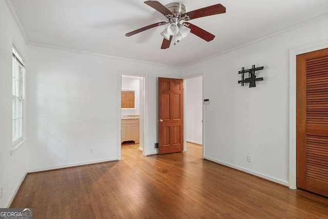 unfurnished bedroom featuring ensuite bath, ceiling fan, wood-type flooring, ornamental molding, and a closet