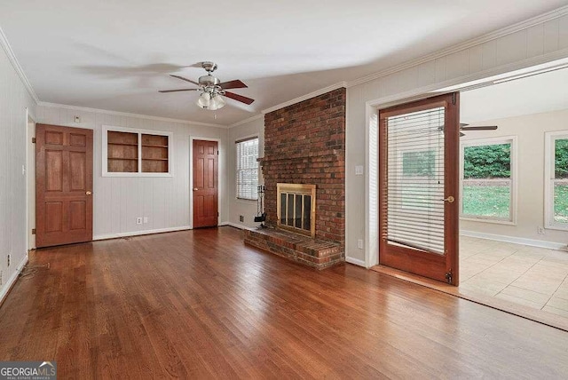 unfurnished living room featuring crown molding, ceiling fan, wood-type flooring, and a brick fireplace