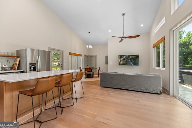 kitchen with stainless steel refrigerator with ice dispenser, a breakfast bar, high vaulted ceiling, hanging light fixtures, and light hardwood / wood-style flooring