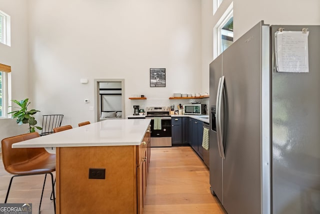 kitchen featuring a kitchen island, appliances with stainless steel finishes, a breakfast bar, a high ceiling, and light hardwood / wood-style flooring