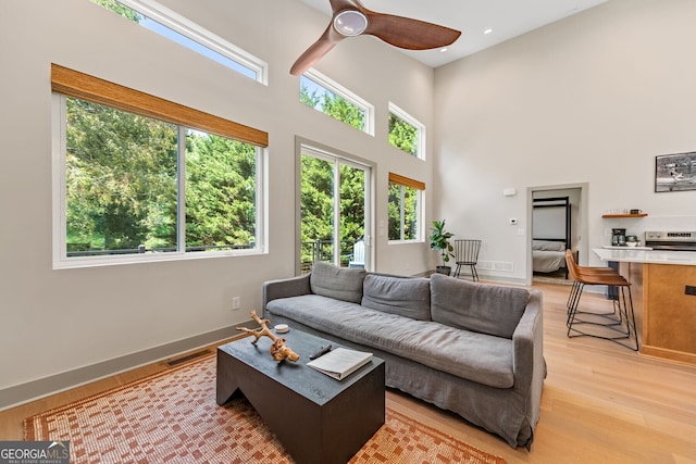 living room with a towering ceiling, light hardwood / wood-style flooring, and ceiling fan