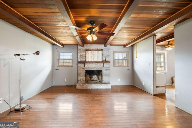 unfurnished living room featuring ceiling fan, hardwood / wood-style floors, beam ceiling, a brick fireplace, and wooden ceiling