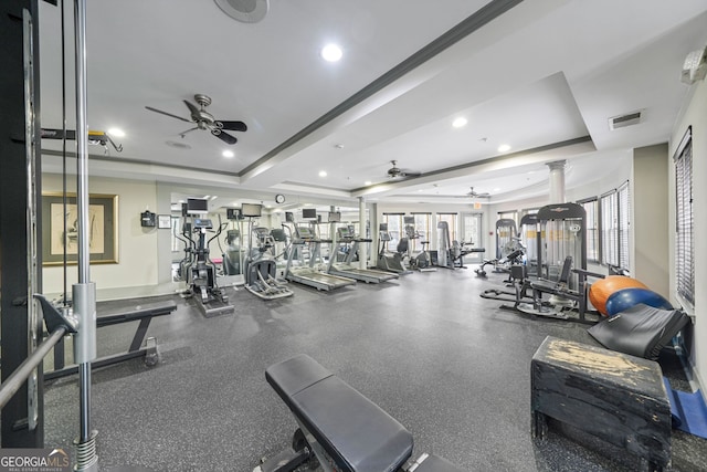 exercise room with a tray ceiling, decorative columns, and ceiling fan