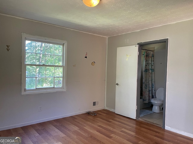 unfurnished bedroom with ensuite bath, wood-type flooring, and a textured ceiling