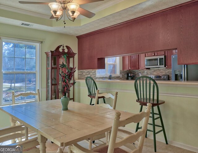 dining space with crown molding, ceiling fan, and a tray ceiling