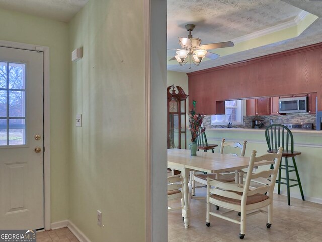 dining space with ornamental molding, a textured ceiling, ceiling fan, and a tray ceiling