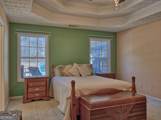 carpeted bedroom with multiple windows, crown molding, and a tray ceiling