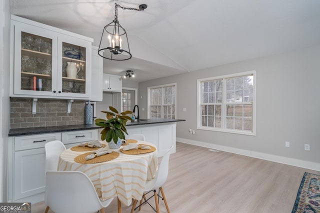 kitchen with pendant lighting, tasteful backsplash, lofted ceiling, sink, and white cabinets