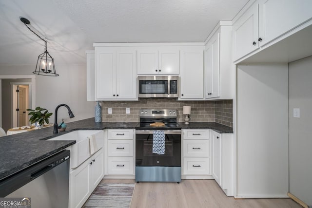 kitchen with pendant lighting, stainless steel appliances, dark stone counters, and white cabinets