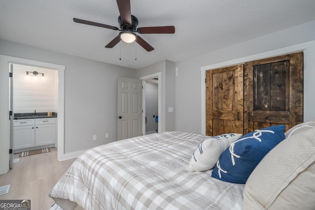 bedroom with ceiling fan, ensuite bath, light hardwood / wood-style flooring, and a textured ceiling