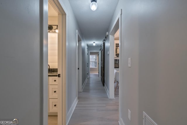 hall featuring a barn door, a textured ceiling, and light wood-type flooring