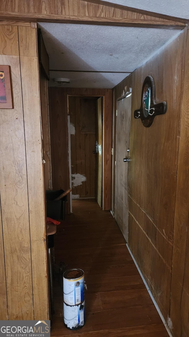 hall with a textured ceiling, dark hardwood / wood-style flooring, and wood walls