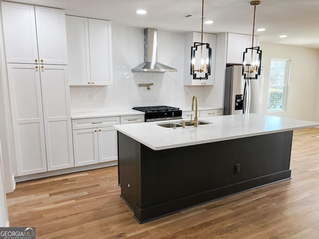 kitchen featuring an island with sink, wall chimney range hood, white cabinets, and stainless steel fridge with ice dispenser