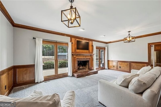 carpeted living room featuring crown molding, a chandelier, and a fireplace