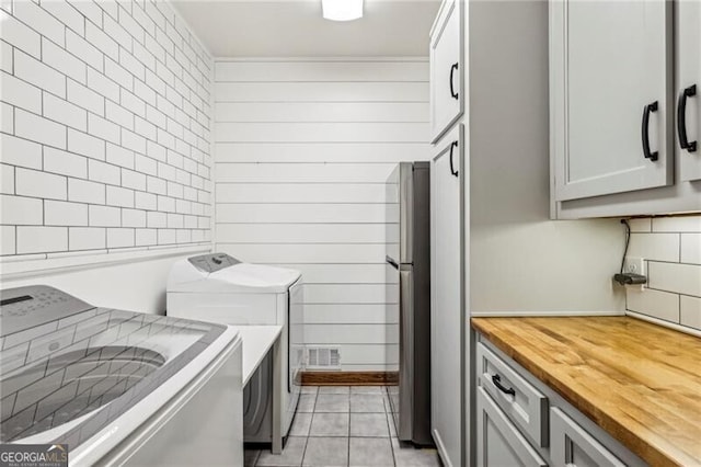 washroom featuring cabinets, wood walls, washer and dryer, and light tile patterned floors