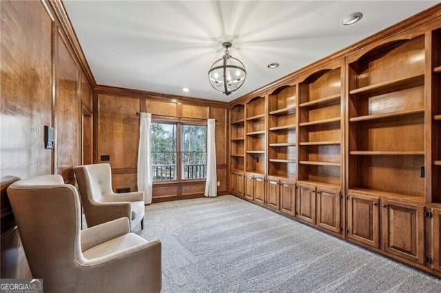 living area with built in shelves, crown molding, light carpet, wooden walls, and a notable chandelier