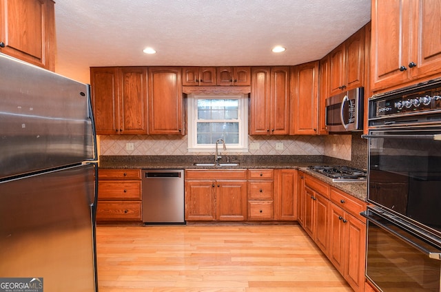 kitchen with sink, dark stone countertops, appliances with stainless steel finishes, light hardwood / wood-style floors, and decorative backsplash